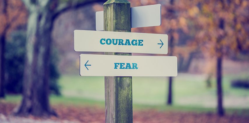Retro style image of a rustic wooden sign in an autumn park with the words Courage - Fear offering a choice of reaction and attitude with arrows pointing in opposite directions in a conceptual image.